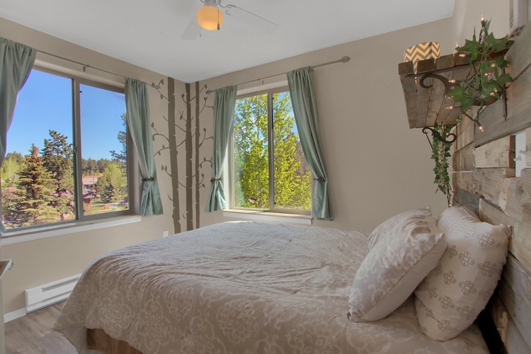 A bedroom with a large bed and a view of trees outside the window.