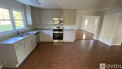 A kitchen with white cabinets and brown tiled floors is available for rent.