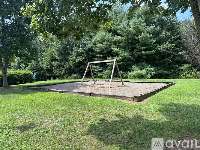 A playground swing set sits in a grassy area surrounded by trees.