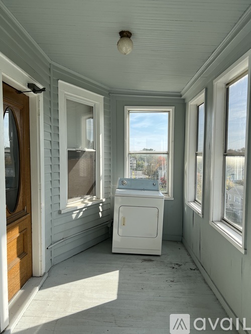 A small white washing machine sits in a sunny room.