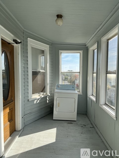 A small white washing machine sits in a sunny room.