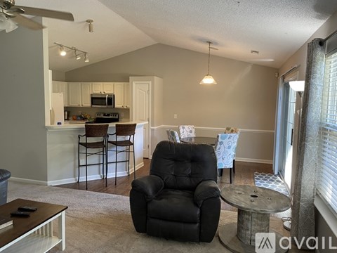 A living room with a black leather chair and a kitchen area in the background.