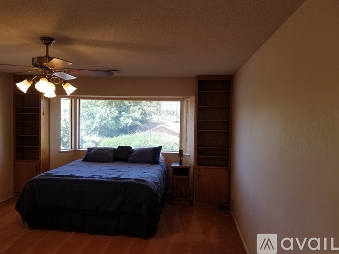 A bedroom with a bed, a ceiling fan, and a window overlooking greenery.