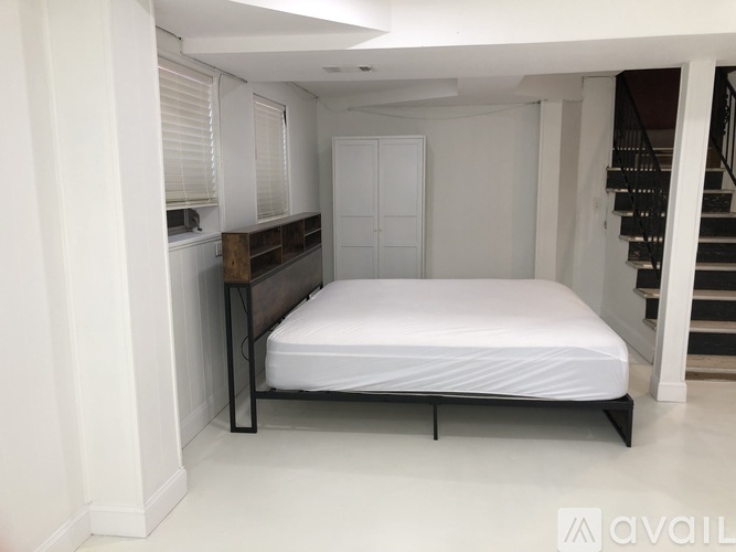 A bedroom with a white bed and a staircase in the background.