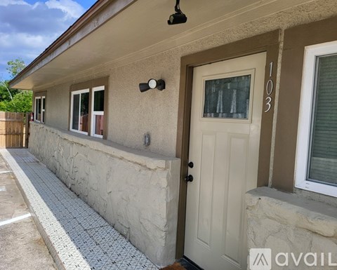 A house numbered 103 has a white door and a stone wall.