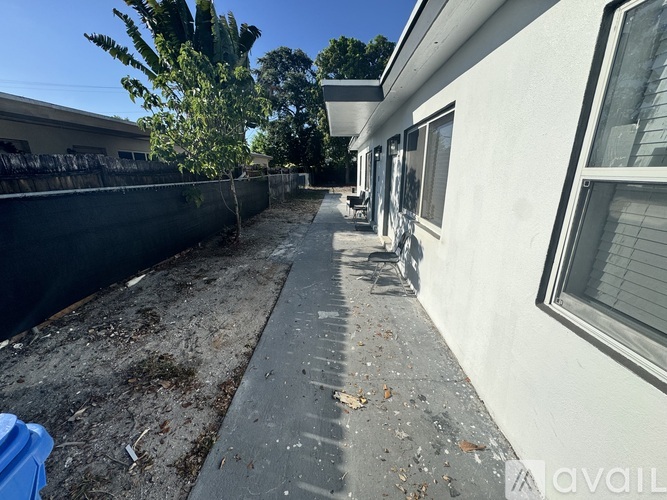 A concrete pathway leads to a white building with a blue container on the ground.