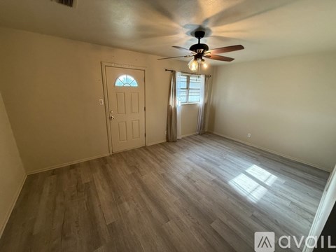 A room with a ceiling fan and light, wooden flooring, and a door with a window.