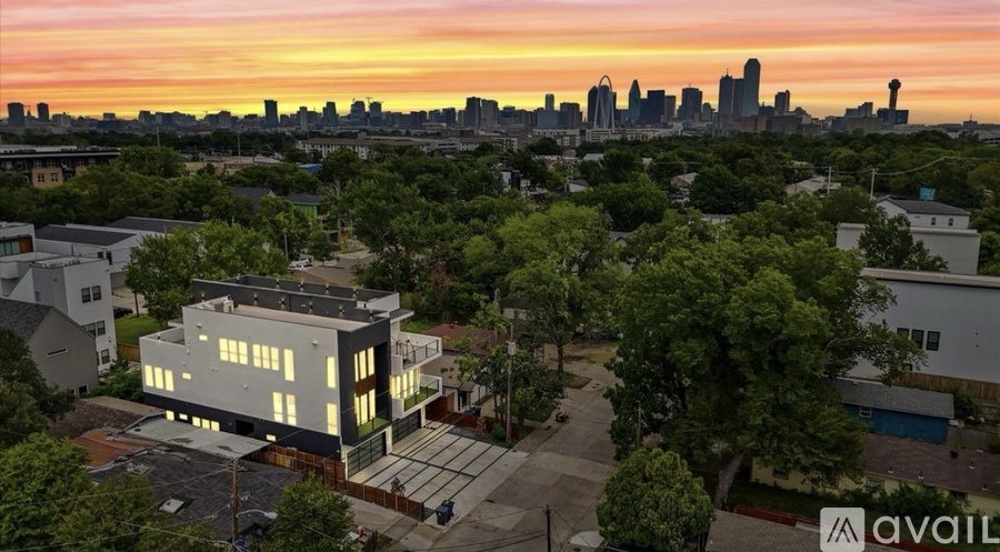 A modern house is for sale in a suburban area with a city skyline at sunset.