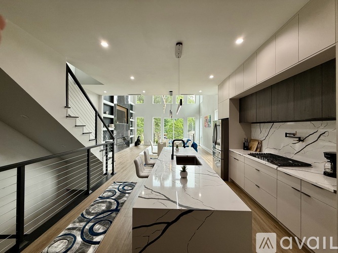 A modern kitchen with a marble countertop and a staircase with a metal railing.