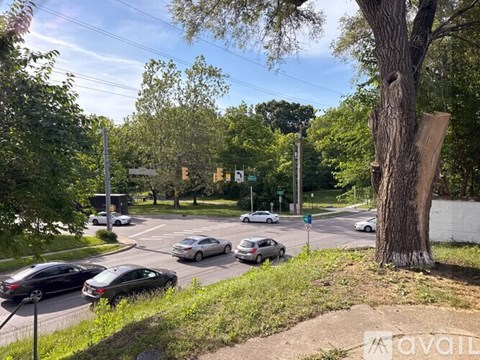 Cars are parked on the side of a road with trees and a traffic light in the background.