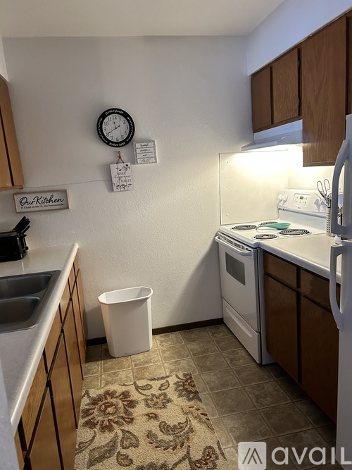 A kitchen with a white trash can and a clock on the wall.