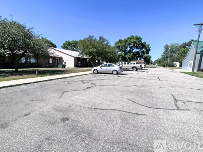 A car is parked in a parking lot with a building and trees in the background.