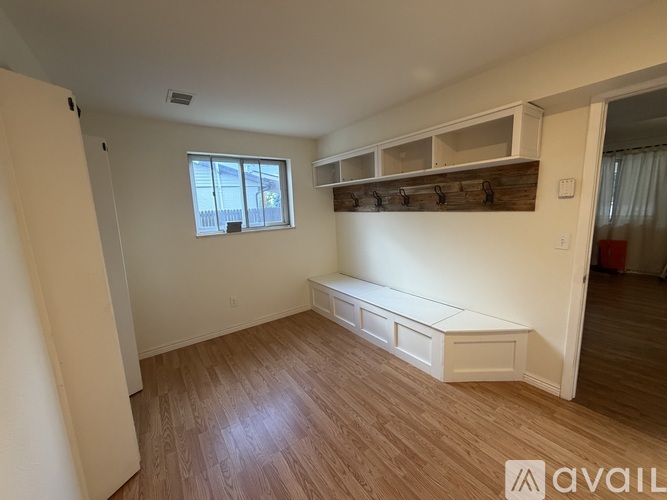 A room with wooden flooring and a window with a view of a fence and trees.