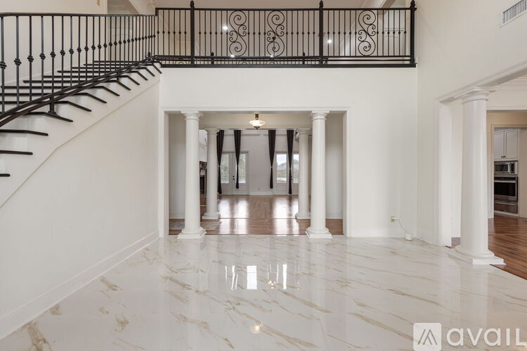 A spacious foyer with a marble floor and a staircase with a black railing.