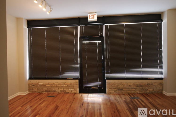 A room with wooden floors and a black door with a window covered in blinds.