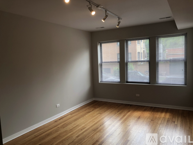 A spacious room with wooden floors and three windows.