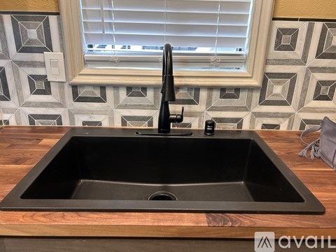A black kitchen sink with a black faucet on a wooden countertop.