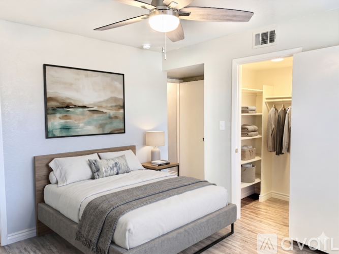 A bedroom with a bed, a ceiling fan, and a painting on the wall.