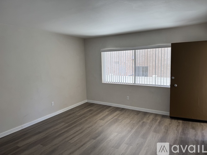 Empty room with wooden flooring and a window with blinds.