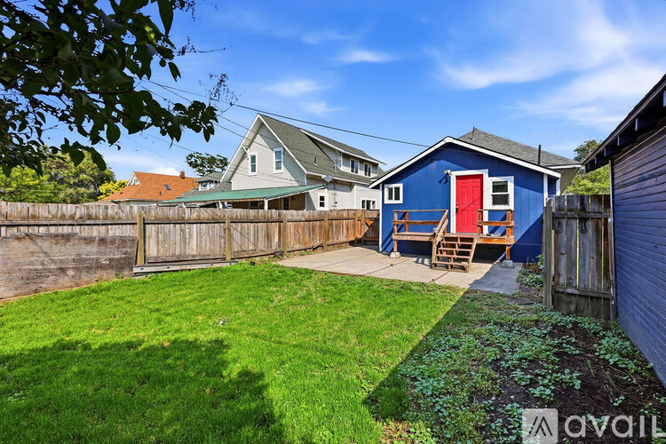 A blue house with a red door is surrounded by a wooden fence and green grass.