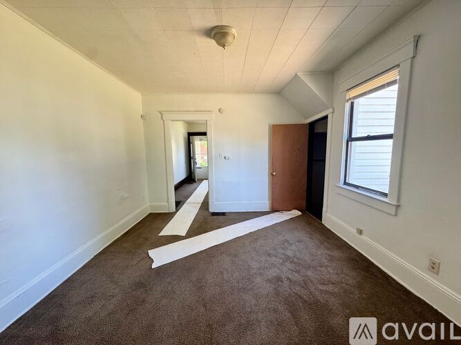 A room with white walls and a brown carpet is available for rent.