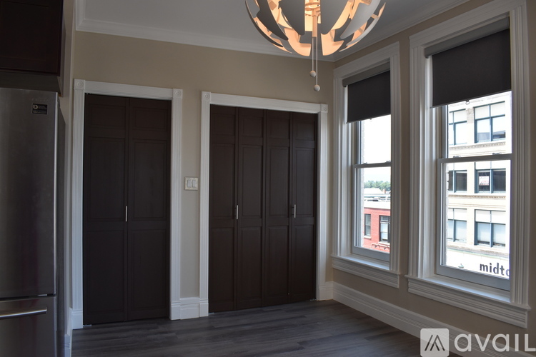 A room with a chandelier, a fridge, and a window showing a building with the word "midt" on it.