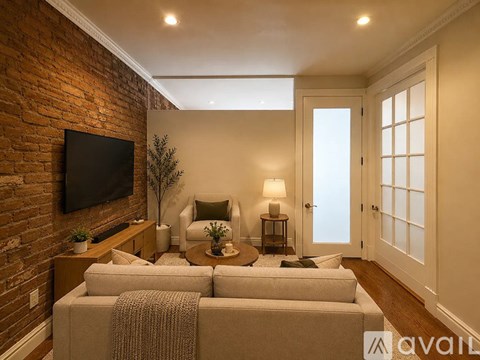 A living room with a couch, a chair, a plant, and a television mounted on a brick wall.