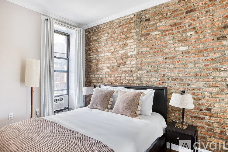 A bedroom with a brick wall and a bed with a white comforter.