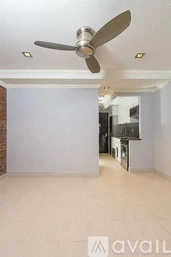 A room with a ceiling fan and a kitchen in the background.