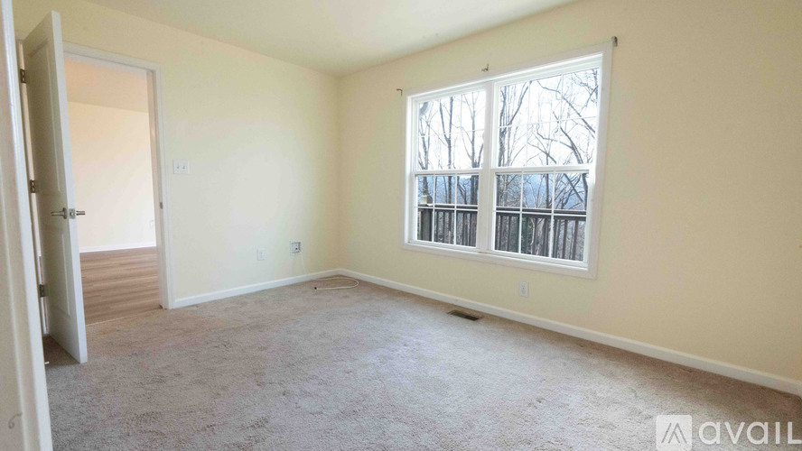 A room with a carpeted floor and a window with a view of a fence and trees.