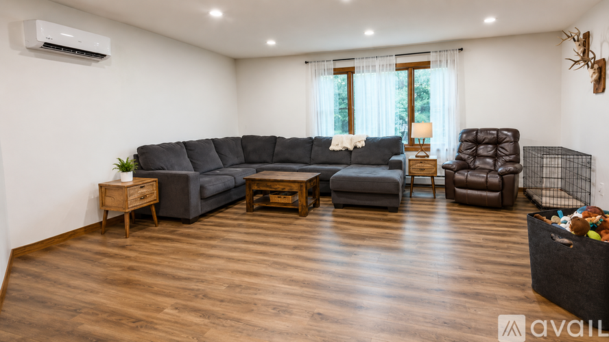 A spacious living room with a grey sectional sofa, a wooden coffee table, and a brown leather armchair.