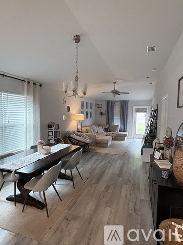 A well-lit, spacious living room with a dining area and a kitchen in the background.