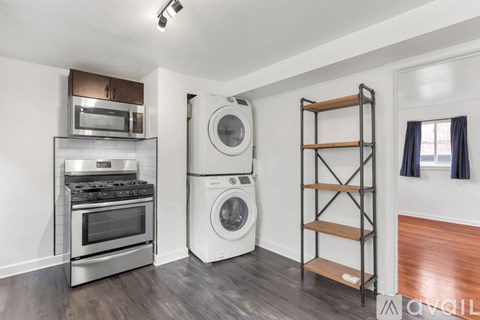 A modern kitchen with a stainless steel oven and microwave, a washing machine, and a wooden shelf.