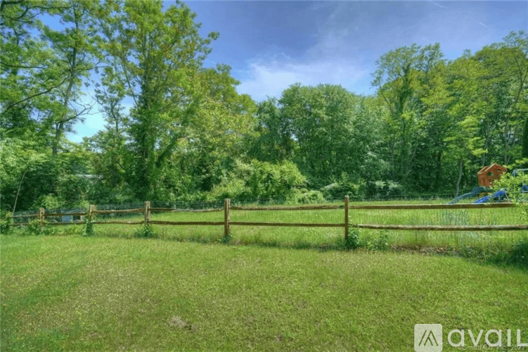 A lush green field with a wooden fence and trees in the background.