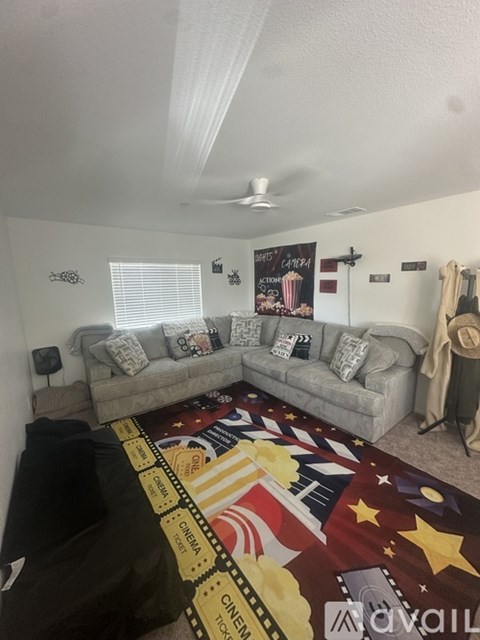 A living room with a grey couch and a rug with a movie theme.