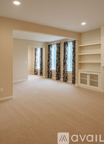 A spacious room with beige carpeting and a row of shelves on one wall.