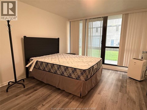 A bedroom with a bed, a window with curtains, and a white air conditioning unit.