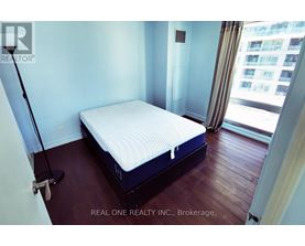 A bedroom with a neatly made bed and a window overlooking a cityscape.