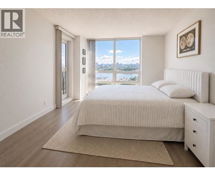 A bedroom with a large bed, a bench, and a view of the city.