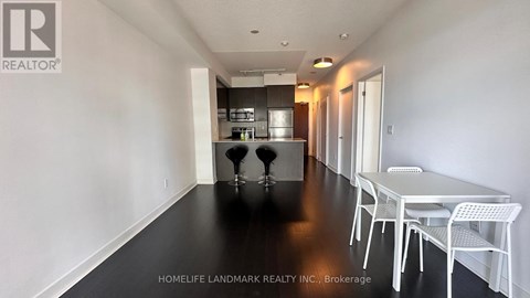 A white dining table with four chairs is in a room with white walls and a kitchen in the background.