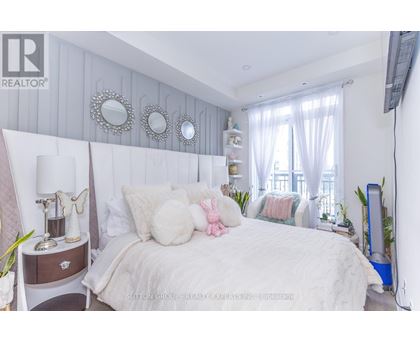 A bedroom with a large bed, a nightstand with a lamp, and a window with curtains.