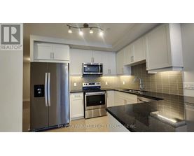 A modern kitchen with a stainless steel refrigerator and black countertops.