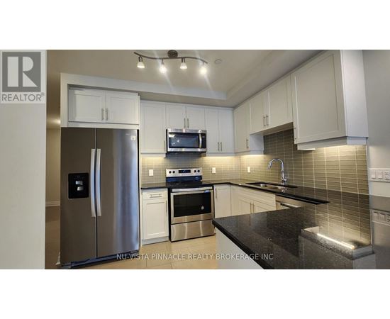 A modern kitchen with a stainless steel refrigerator and black countertops.