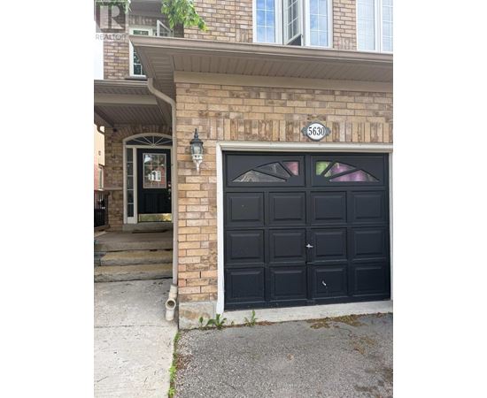 A black garage door with a white number 6630 on the brick wall above it.