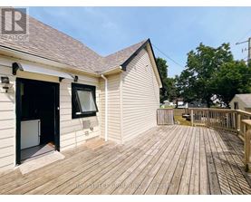 A wooden deck is attached to a white house with a black door and window.