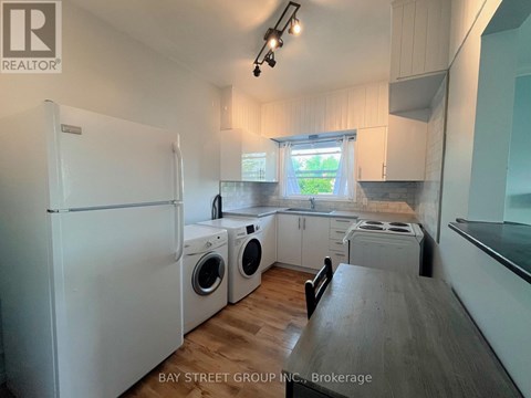 A white refrigerator is in a kitchen with wooden floors and white cabinets.