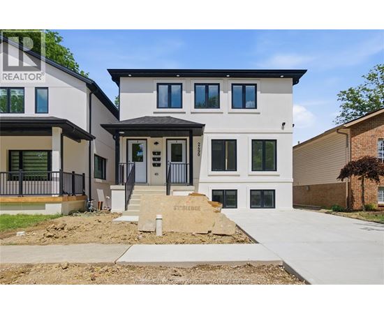 A modern two-story house with a realtor sign on the front.