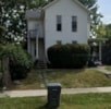 A white house with a black trash can in front of it.