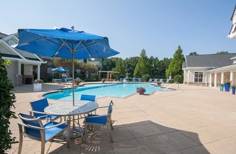 A blue umbrella is next to a table and chairs by a pool.