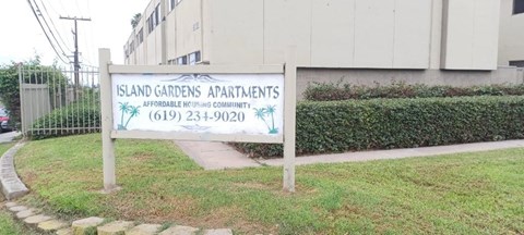 A sign for Island Gardens Apartments is displayed in front of a building.